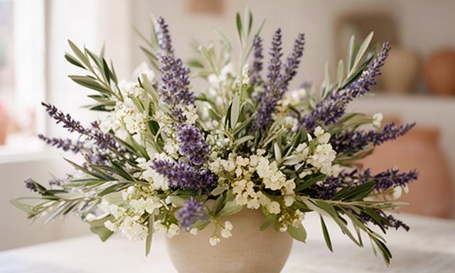 Composizione floreale mediterranea con lavanda, ulivo e fiori chiari su un tavolo luminoso